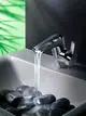 Waschtischarmatur von Ideal Standard mit Wasserfallauslauf, montiert über schwarzen Steinen in einem modernen Waschbecken. Chromoberfläche spiegelt Licht wider.
